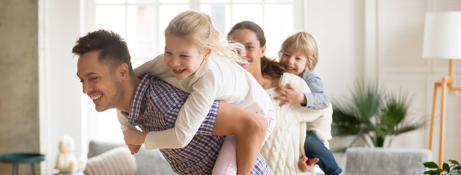Happy loving dad piggybacking little daughter playing with family at home, smiling parents carrying kids on back, children boy and girl having fun together enjoying ride during active game on weekend