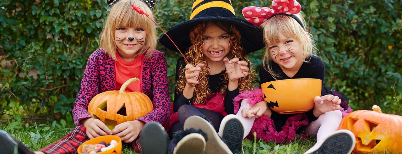 friendly-kids-with-symbols-of-halloween-sitting-on-grass-SBI-321748146